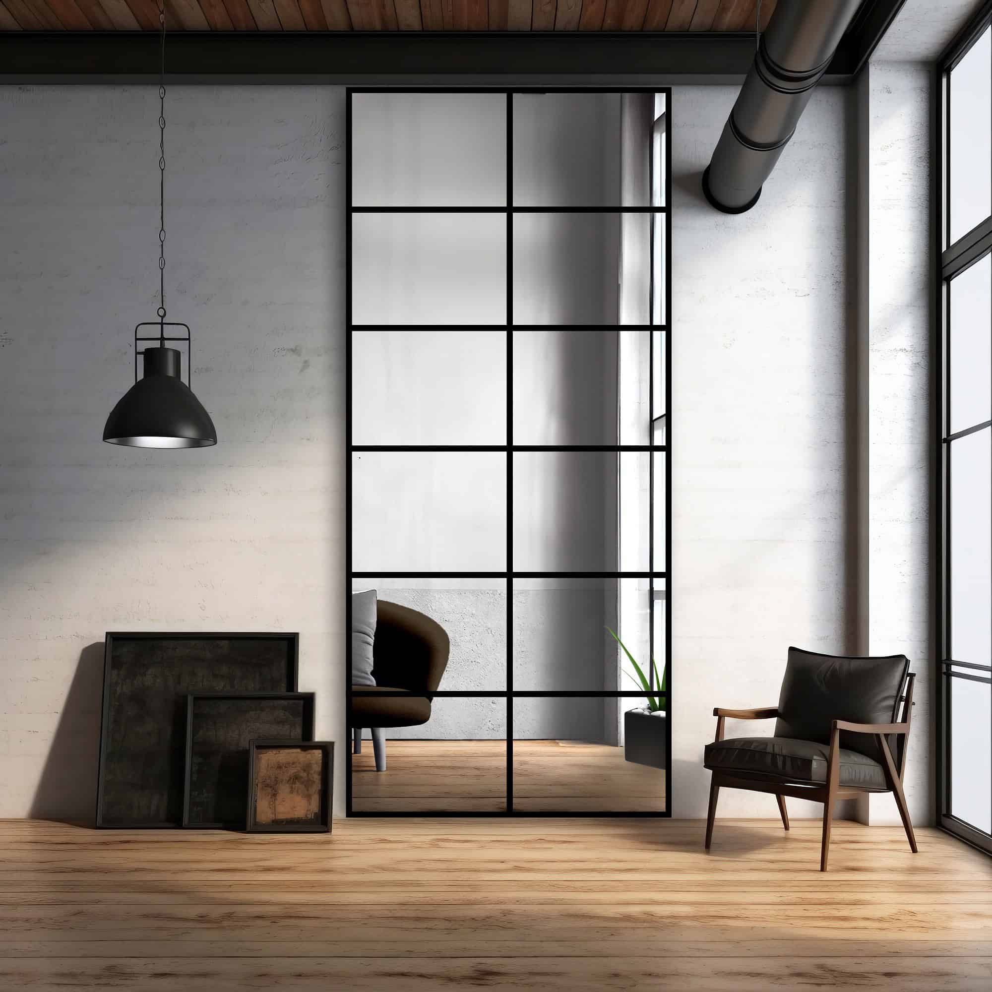 Oglindă mare în stil industrial cu ramă din oțel negru și grilaj metalic, sprijinită de un perete din beton într-un interior modern, cu podea din lemn și accente minimaliste.
